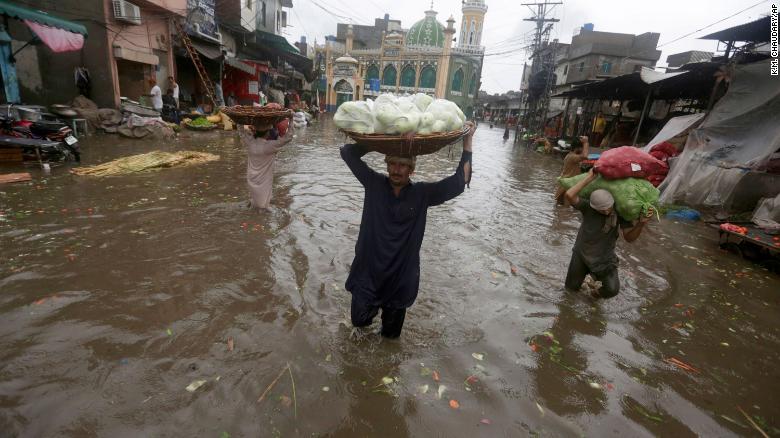 Laborers carry produce as they wade through a flooded road after heavy rainfall, in Lahore, Pakistan, Thursday, July 21, 2022. 